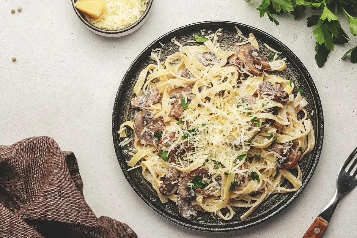 Un piatto invitante di tagliatelle ai porcini, condite con una cremosa salsa e abbondante parmigiano grattugiato.
