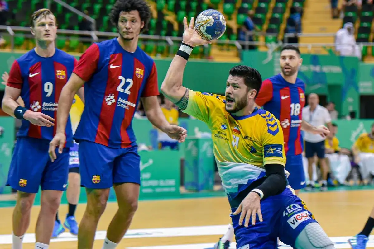 Piłkarz ręczny w żółtej koszulce rzuca piłkę, podczas gdy zawodnicy FC Barcelona w niebiesko-czerwonych strojach obserwują. Vive Barcelona!
