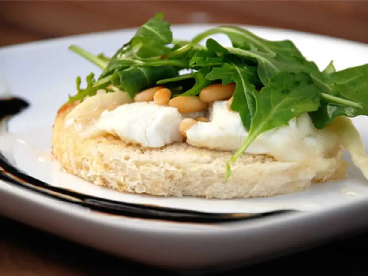 En bit rostat bröd med smält **chevre chaud**, pinjenötter och ruccola. En läcker förrätt.