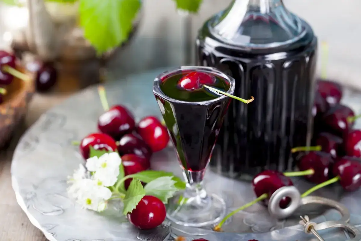 Szklaneczka z ciemnym likierem, ozdobiona wiśnią, obok butelka i świeże owoce. Pyszne owoce w alkoholu.