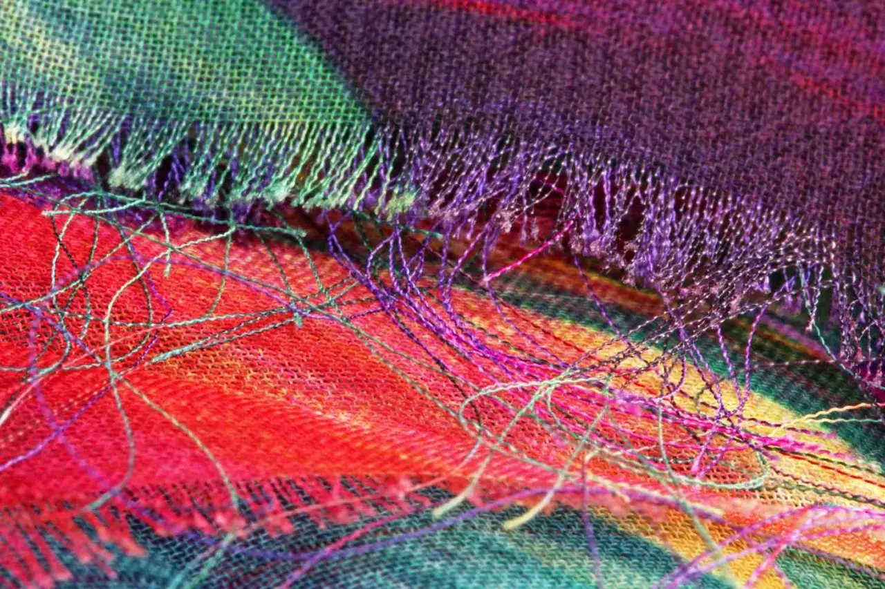 Close-up of a colorful woven fabric, showing how the threads fray. The vibrant red, green, and purple threads create a beautiful, textured pattern.