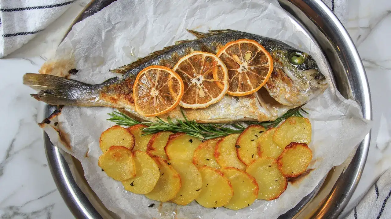 Orata in friggitrice ad aria, dorata e succulenta, servita con patate croccanti e fette di limone caramellato.