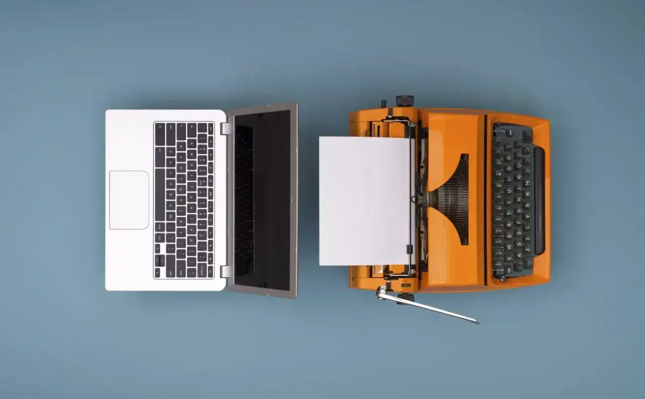 Un port&aacute;til y una m&aacute;quina de escribir naranja, uno al lado del otro, ilustran la evoluci&oacute;n de la escritura y el concepto de que es digitalizaci&oacute;n.