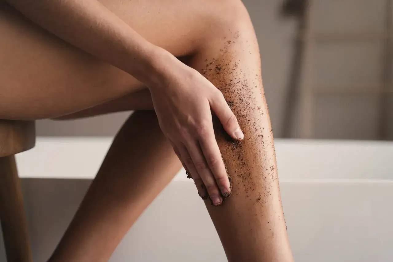 Dłoń rozprowadza peeling kawowy po nodze. Idealny rytuał: najpierw peeling czy golenie?