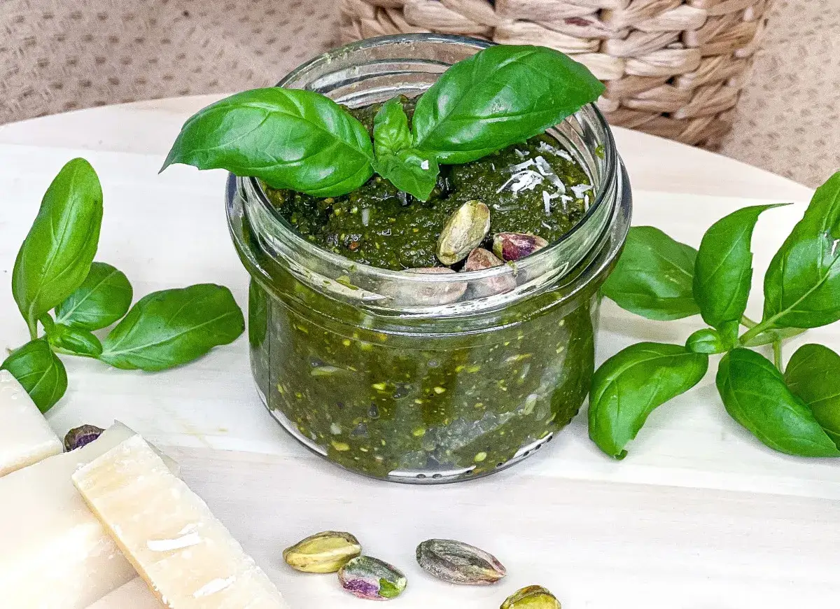 Słoik domowego pesto pistacjowego z bazylią i parmezanem, ozdobiony świeżymi listkami i łuskanymi pistacjami.
