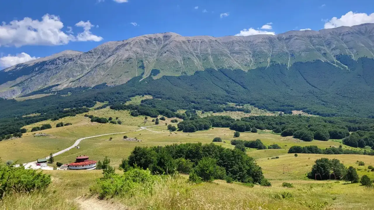 Vasta distesa verde ai piedi del monte Mileto, con un edificio circolare rosso e una strada che serpeggia tra i prati.