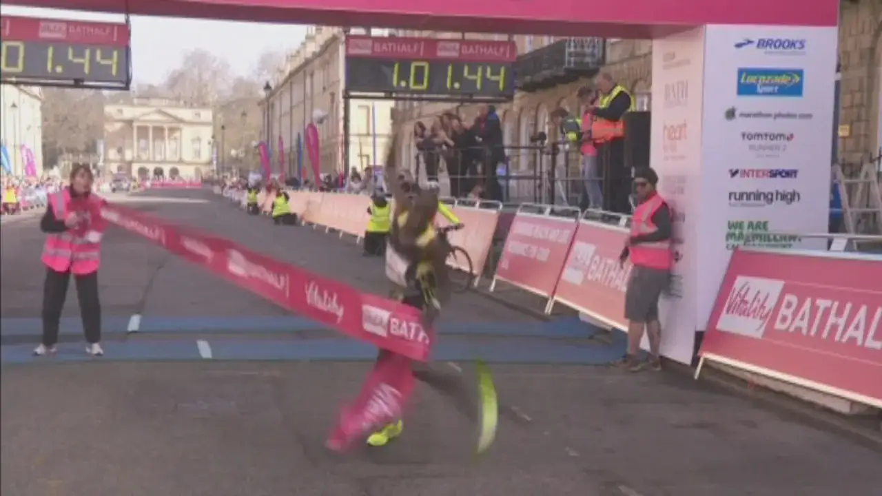 Biegacz przekracza linię mety, celując w maraton poniżej 2h. Czas na tablicy: 1:44.