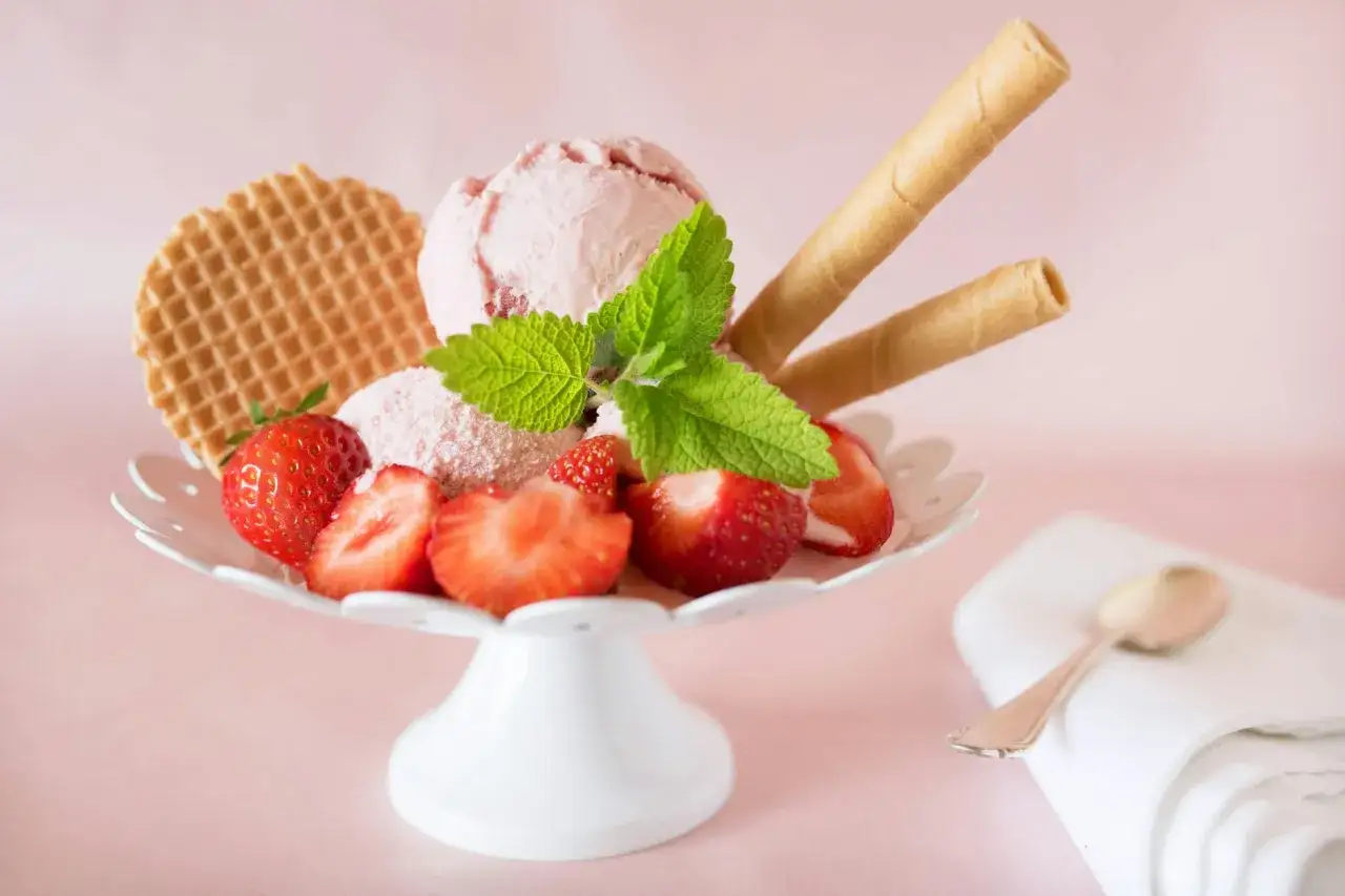 Ein köstliches schnelles Erdbeereis mit frischen Erdbeeren, Minze und Waffelröllchen auf einem weißen Eisbecher.