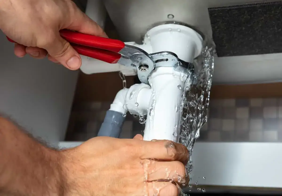 Mains pour colmater une fuite d'eau sous un &eacute;vier, utilisant une pince pour serrer un raccord de tuyau qui goutte.