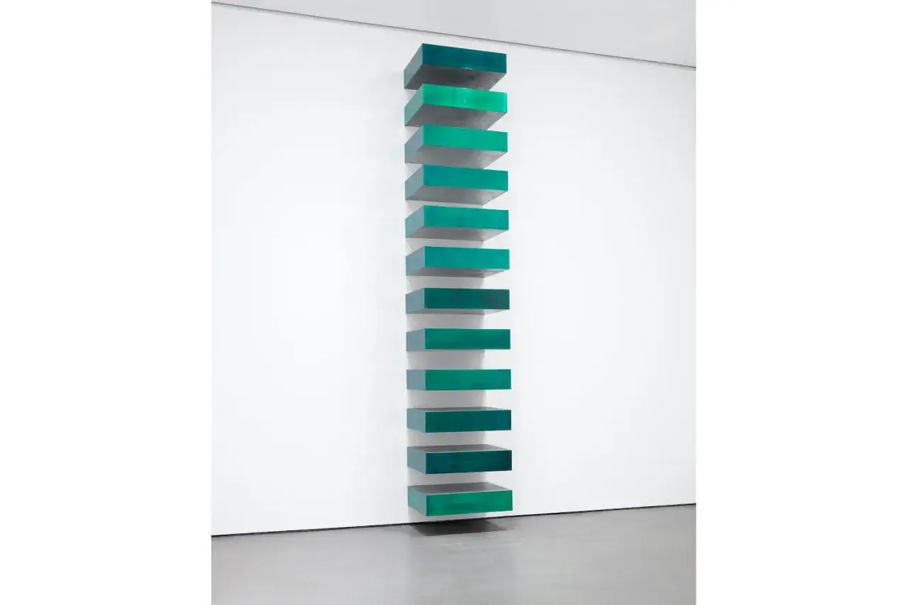 Installazione verticale di 11 parallelepipedi verdi e blu, tipica di Donald Judd, che sembrano galleggiare sulla parete bianca.