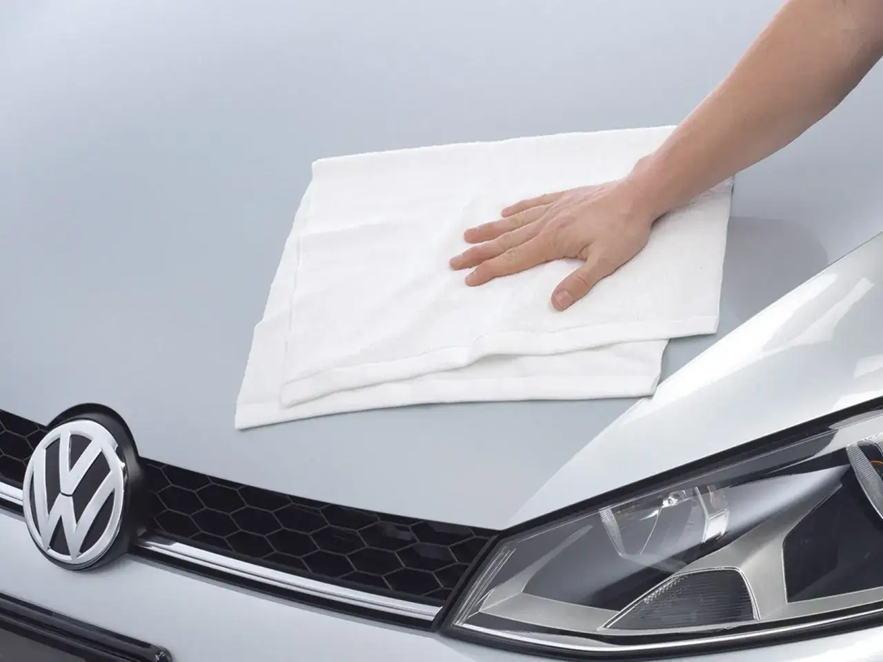 Dłoń z białą ściereczką na masce Volkswagena. Szybka aplikacja produktu do pielęgnacji auta.