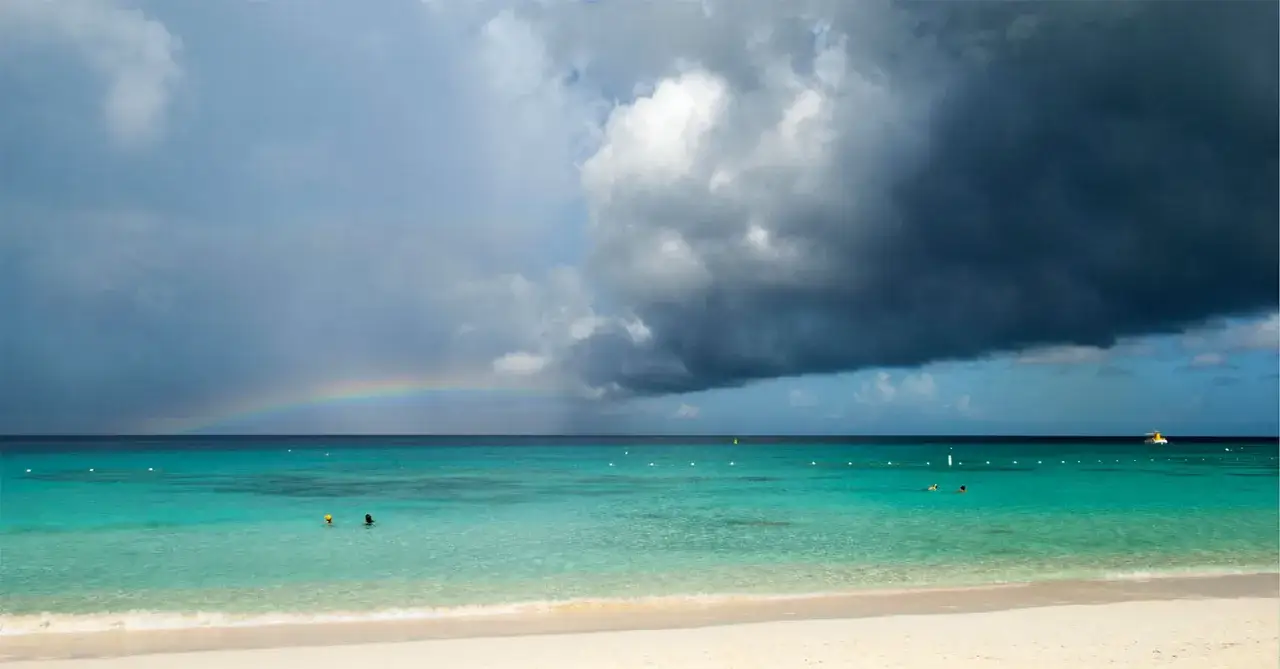 Tropikalna plaża z turkusową wodą, tęczą i burzowymi chmurami. To piękny widok, mimo że to phuket pora deszczowa.