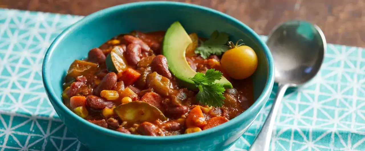 Herzhaftes Chili sin Carne in einer blauen Sch&uuml;ssel, garniert mit Avocado, Koriander und einer gelben Tomate.