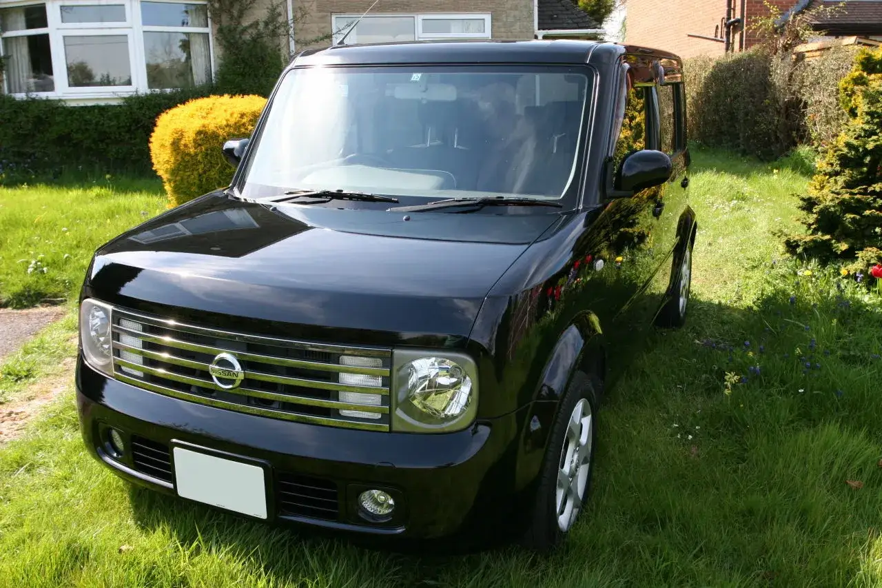 Czarny Nissan Cube błyszczy w słońcu na trawiastym podwórku.