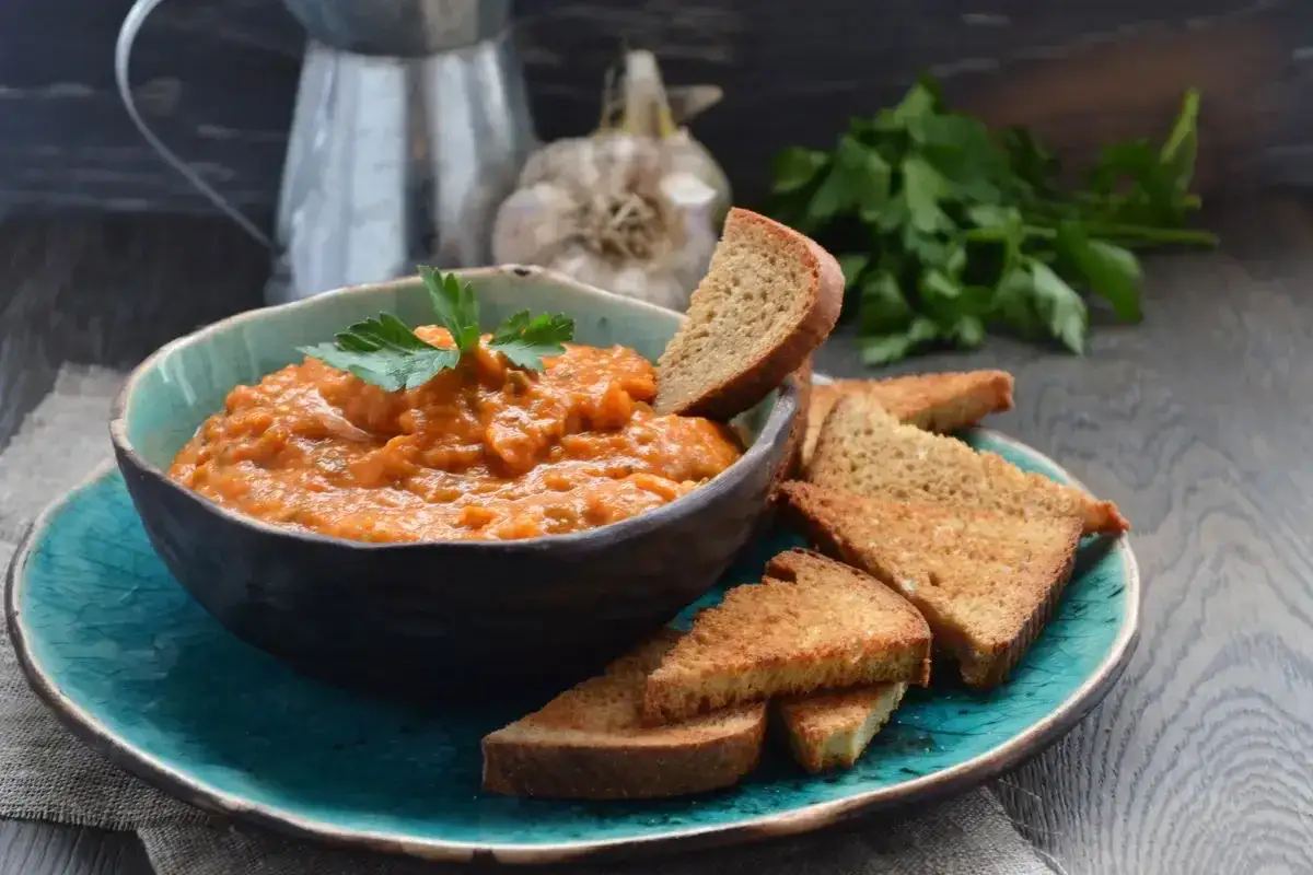 Pesto di melanzane fatto col Bimby, servito in ciotola con crostini di pane tostato e guarnito con prezzemolo fresco.
