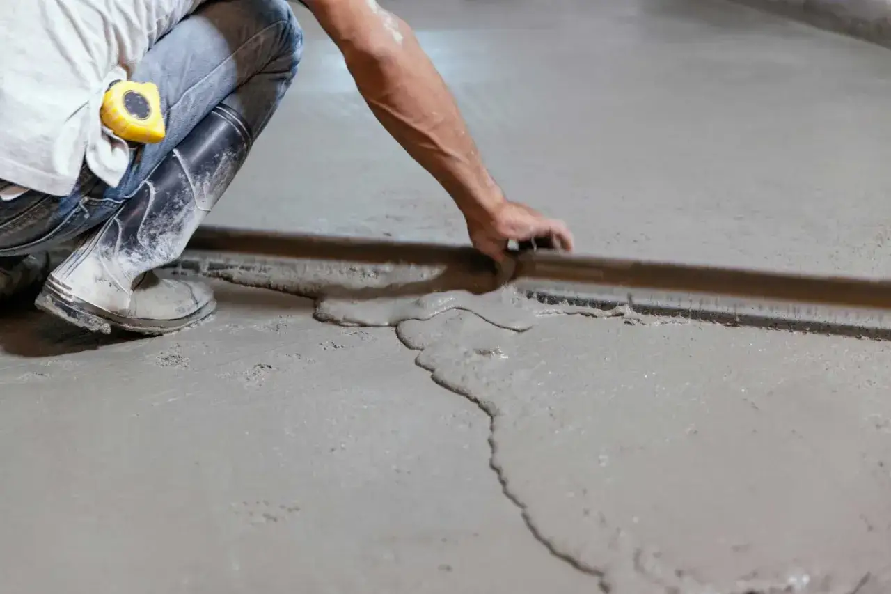 Operaio con stivali e metro lavora per livellare pavimento in pendenza con una staggia, creando una superficie liscia.