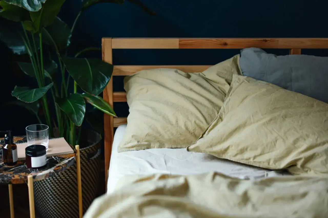 A rumpled bed with light yellow pillows and a grey pillow. A bedside table holds a glass of water, a notebook, and a bottle. Is it normal to toss and turn in your sleep?
