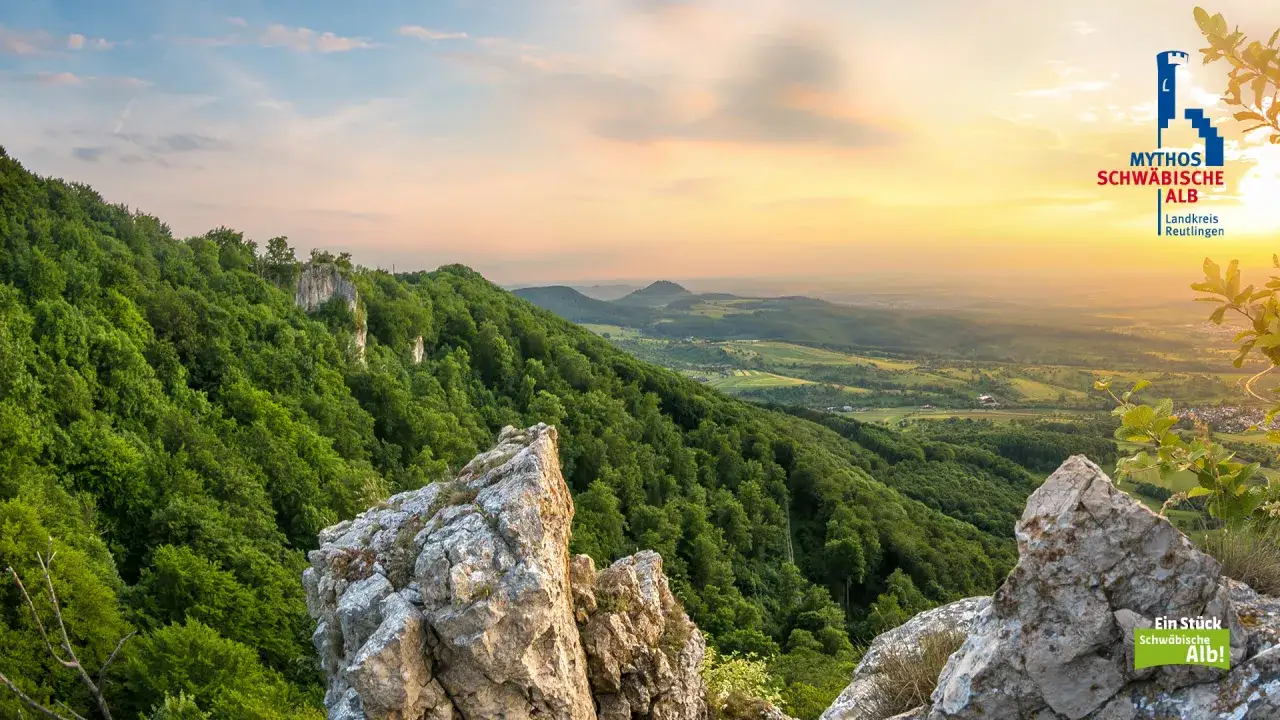 Sonnenuntergang über bewaldeten Hügeln im Landkreis Reutlingen. Felsen im Vordergrund, im Hintergrund eine weite Landschaft.