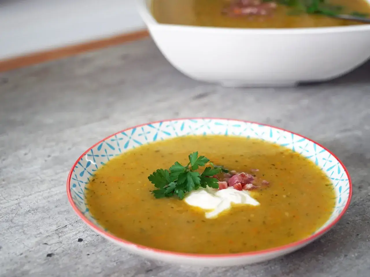 Eine cremige Kartoffelsuppe, zubereitet im Thermomix, garniert mit einem Klecks Sahne, Petersilie und Speckwürfeln.