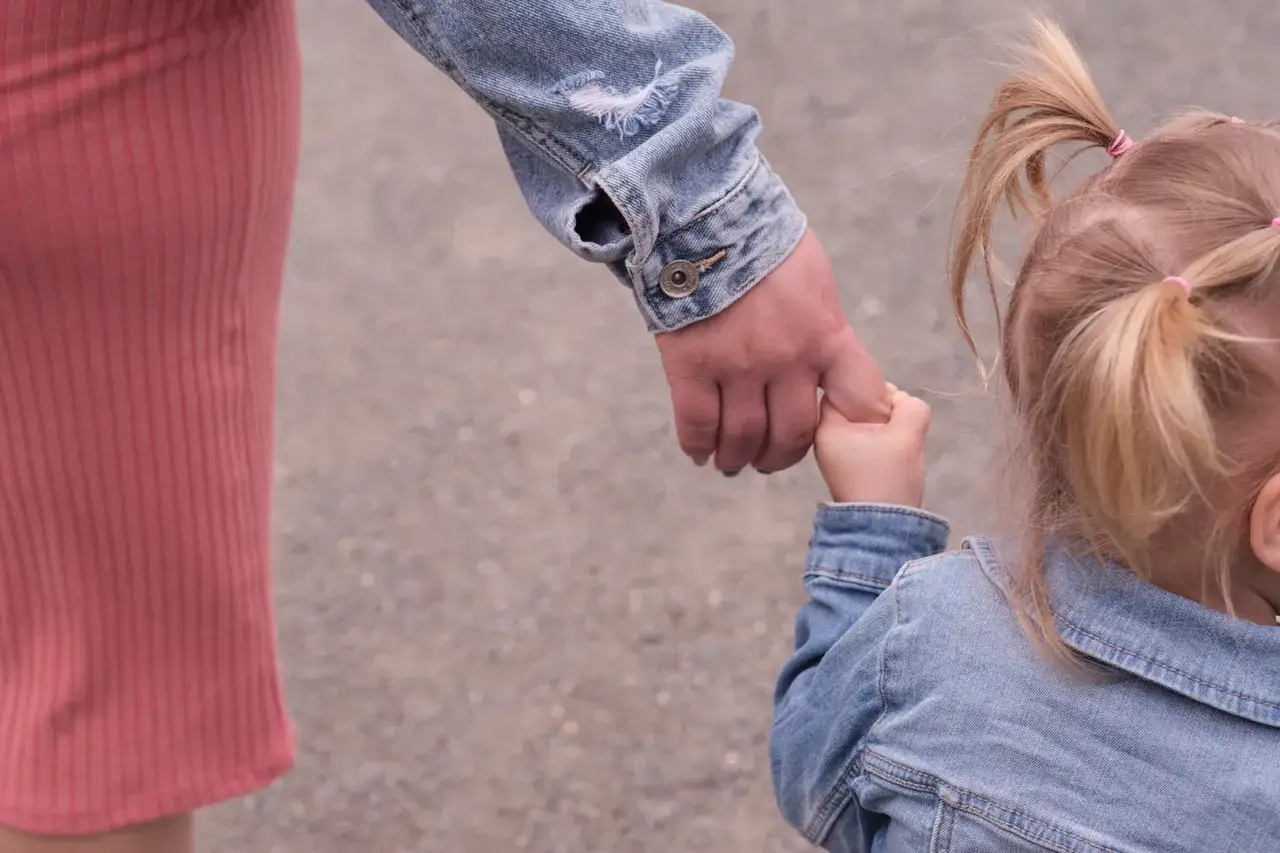 Mama i dziecko trzymają się za ręce. Dziecko ma blond kucyki i jeansową kurtkę. To inspiracja, jak ubrać dziecko na sesję zdjęciową.