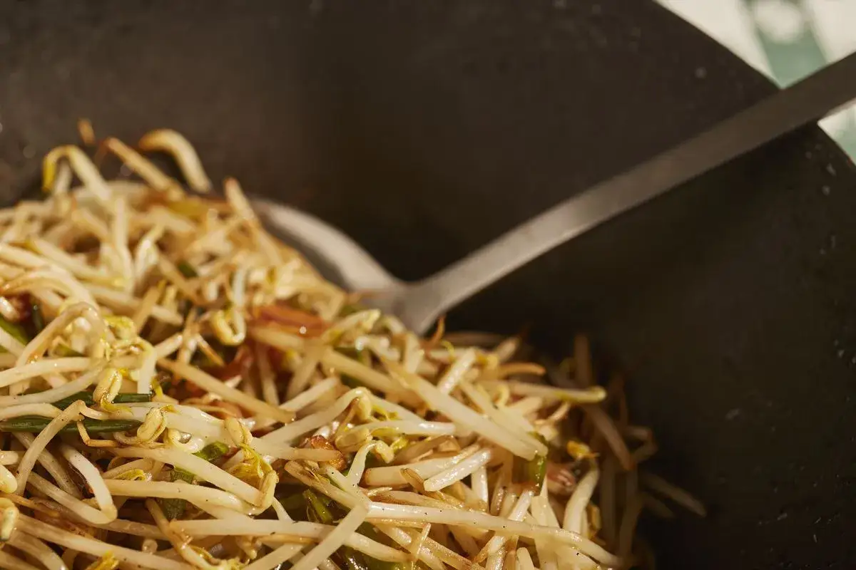 Germogli di soia saltati in padella, con una spatola che li mescola in un wok.