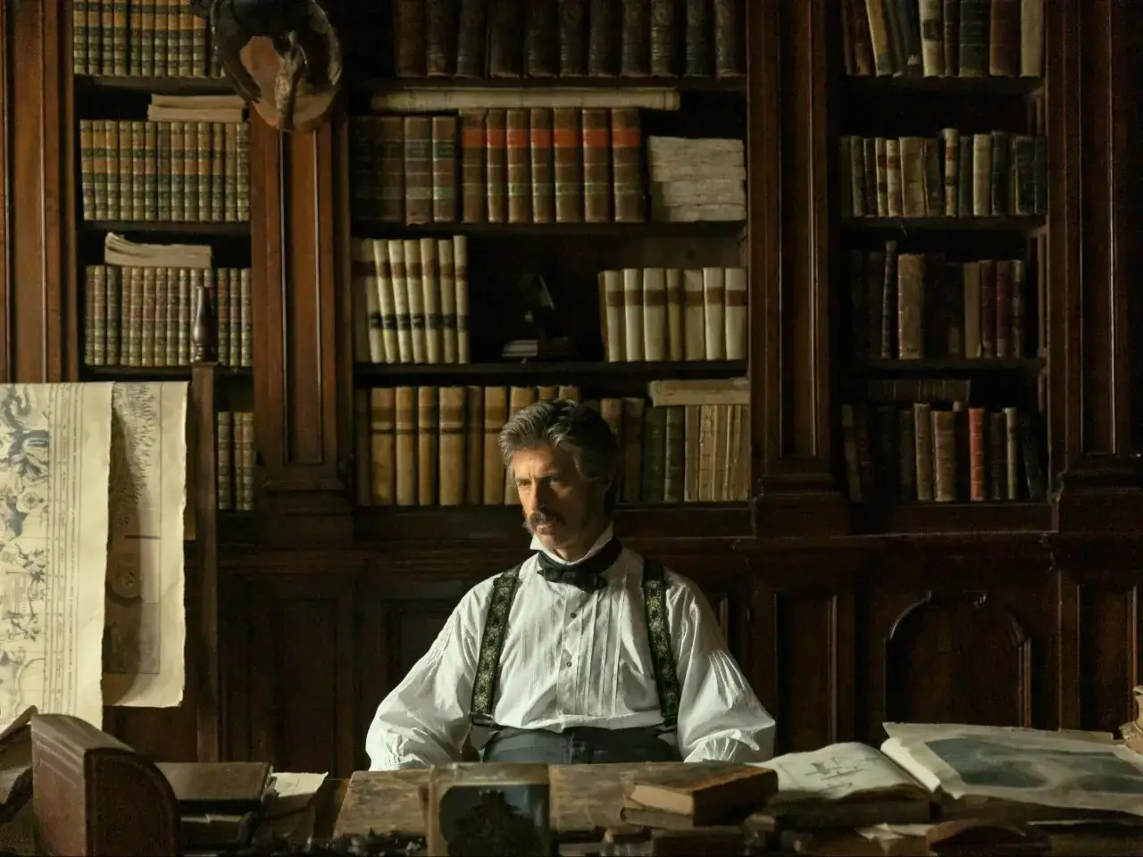 Mężczyzna w historycznym stroju siedzi w bibliotece pełnej książek, które mogą posłużyć jako inspiracja do seriali na podstawie książek.