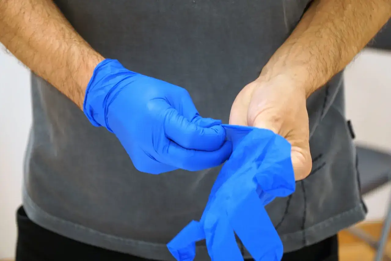 Person zieht blaue Einweghandschuhe an. Diese sind Teil der pflegehilfsmittel zum verbrauch liste f&uuml;r Hygiene.