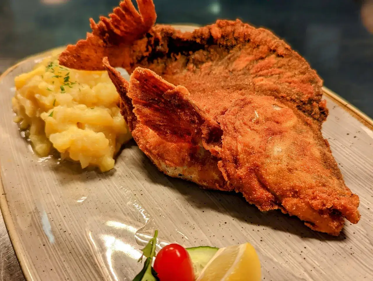 Knusprig gebackener Karpfen mit Kartoffelpüree, garniert mit Petersilie, Zitrone und Tomate.