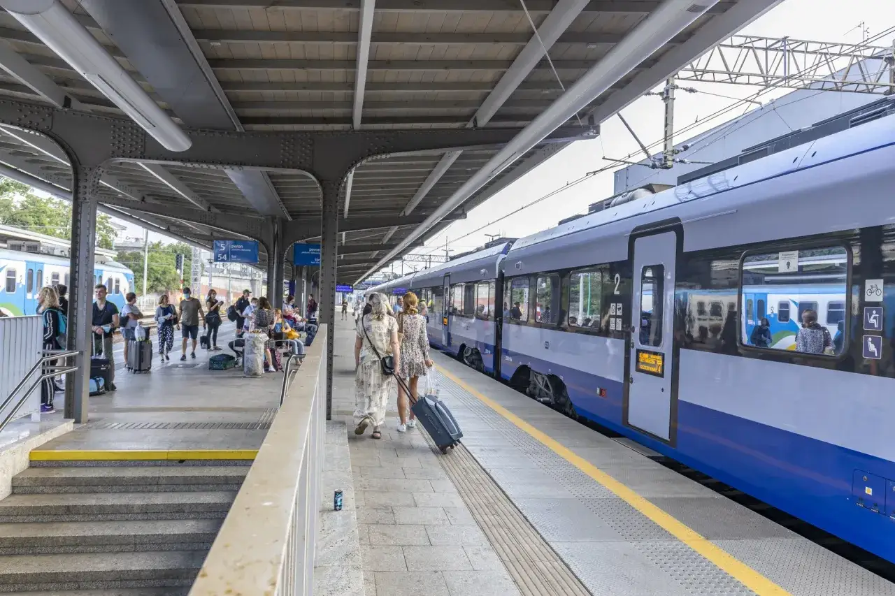Ludzie z bagażami czekają na peronie na poznańskim dworcu kolejowym. Pociąg stoi przy peronie.