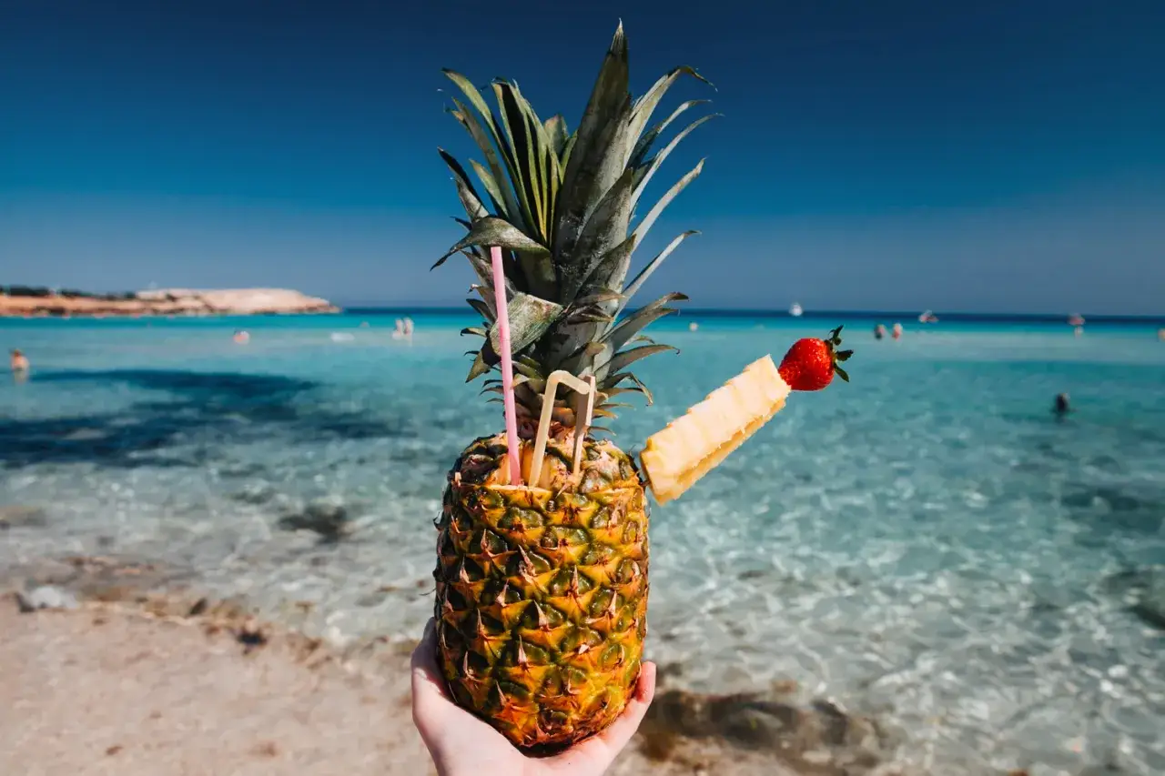 Ananasowy drink na plaży, idealny po podr&oacute;ży z Larnaki do Ayia Napa. Błękitne morze i słońce.