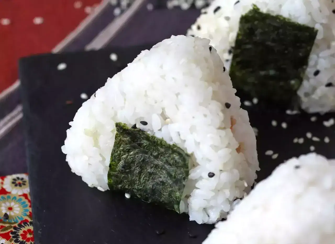Tr&oacute;jkątne onigiri z ryżu, posypane sezamem, z kawałkami nori. Idealne na szybki lunch, jak w prostym onigiri przepisie.