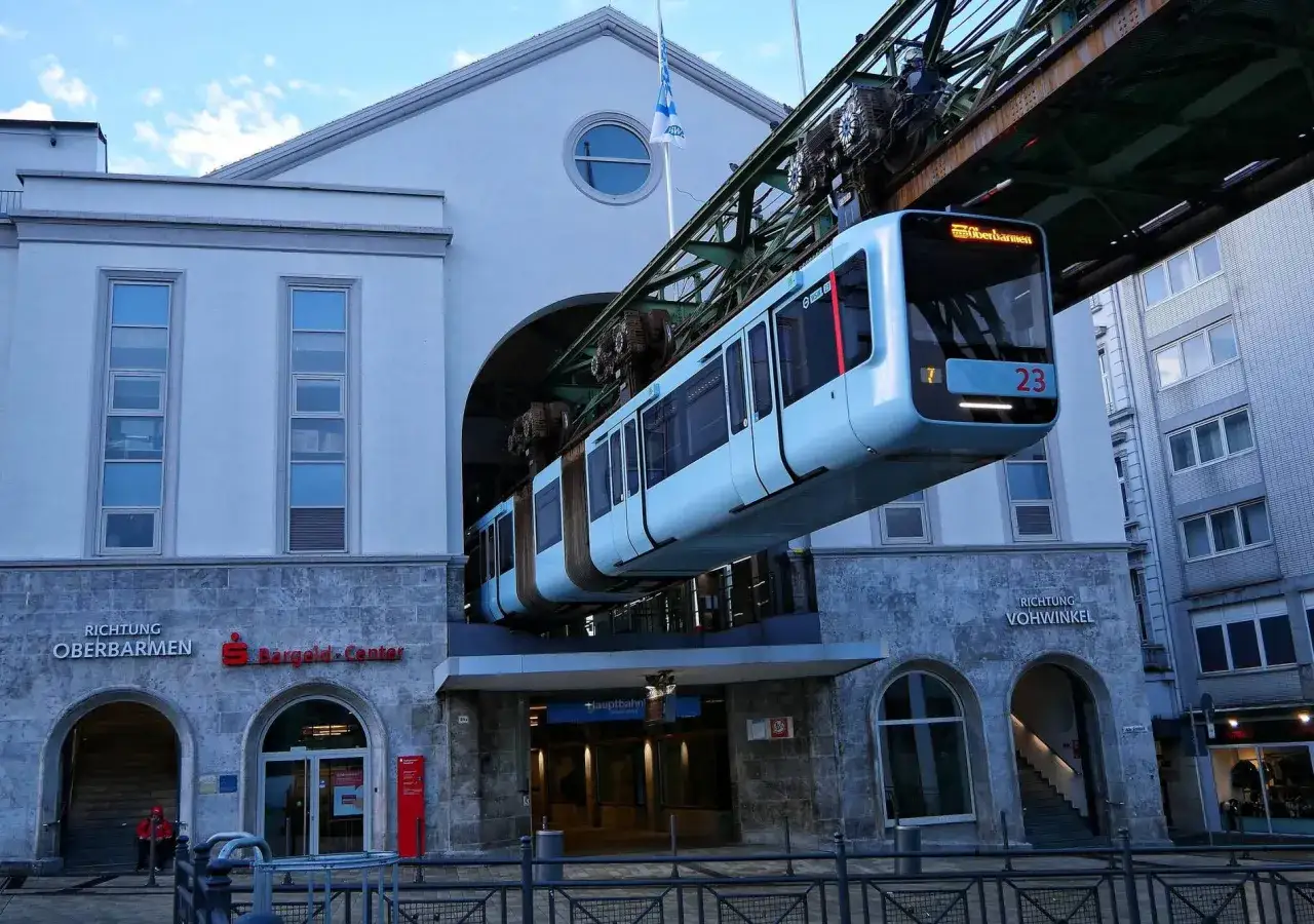 Eine Schwebebahn f&auml;hrt &uuml;ber den **Wuppertaler Hauptbahnhof**. Das blaue Gef&auml;hrt mit der Nummer 23 ist auf dem Weg nach Oberbarmen.
