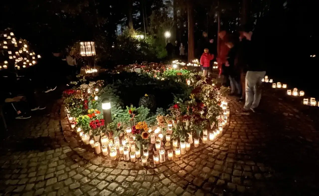M&aring;nga ljus lyser upp en gravplats under all helgons dag. Blommor och m&auml;nniskor syns i m&ouml;rkret.