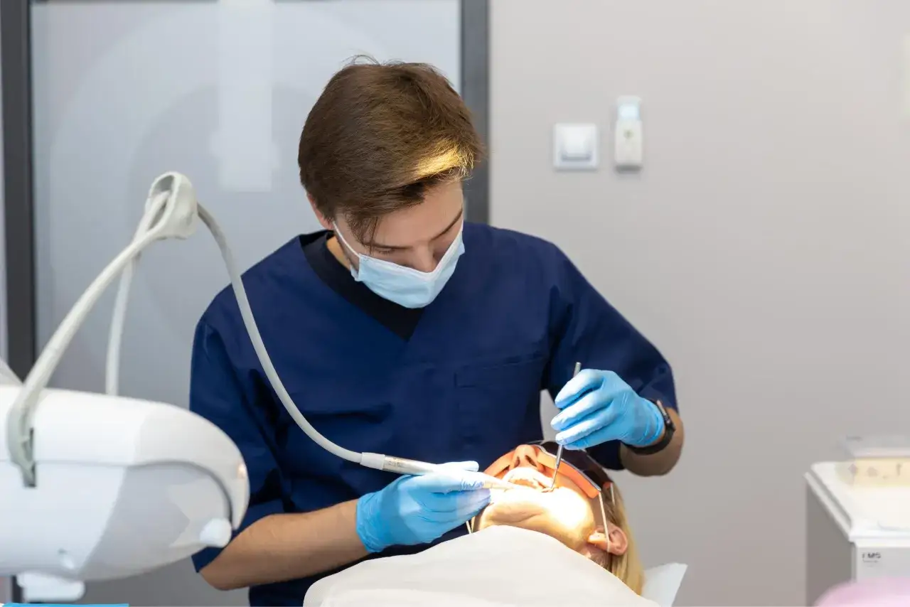 Dentysta w niebieskim fartuchu i masce wykonuje zabieg. Pacjentka leży na fotelu, czując lekkie szybkie bicie serca po znieczuleniu u dentysty.