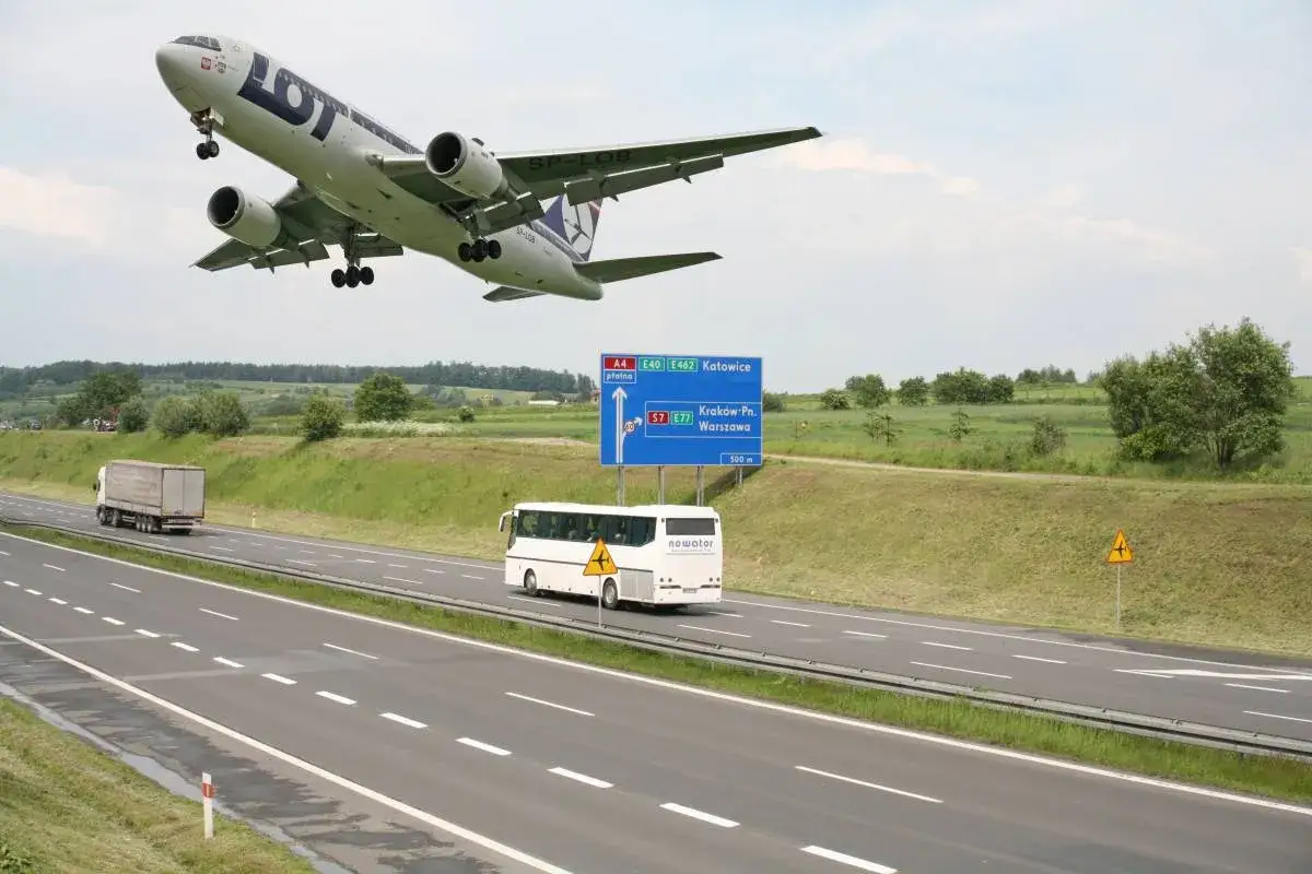 Samolot LOT-u nisko nad autostradą A4 w kierunku Katowic. Obok znak drogowy wskazujący drogę do Krakowa i Warszawy.