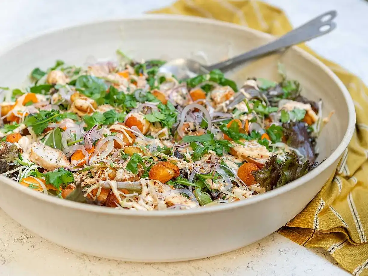 En stor skål med en matig sallad fylld med kyckling, sötpotatis, grönsaker och en krämig dressing.