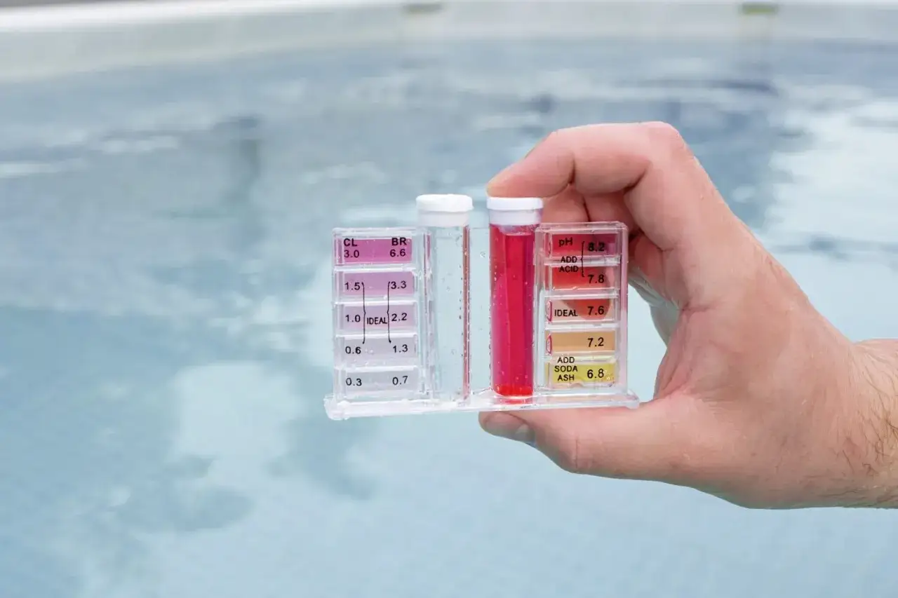 Hand hält Pool-Testgerät zur Überprüfung der Chlordosierung und des pH-Werts. Die roten Flüssigkeiten zeigen die Ergebnisse an.