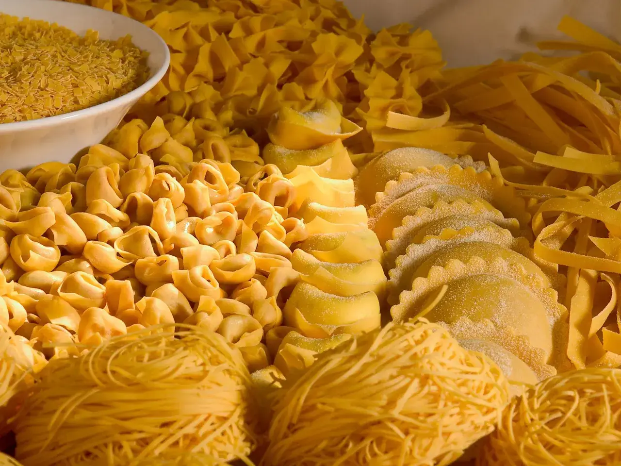 Varietà di pasta fresca, tra cui tortellini, ravioli e tagliatelle, che rappresentano i cibi tipici dell'Emilia Romagna.