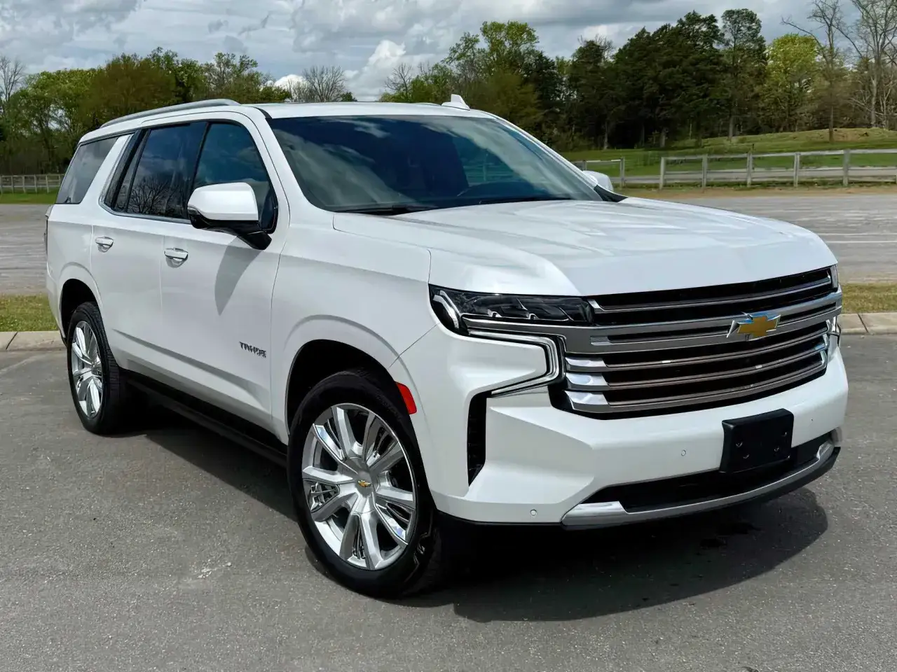 Biały Chevrolet SUV Tahoe lśni na tle zieleni.