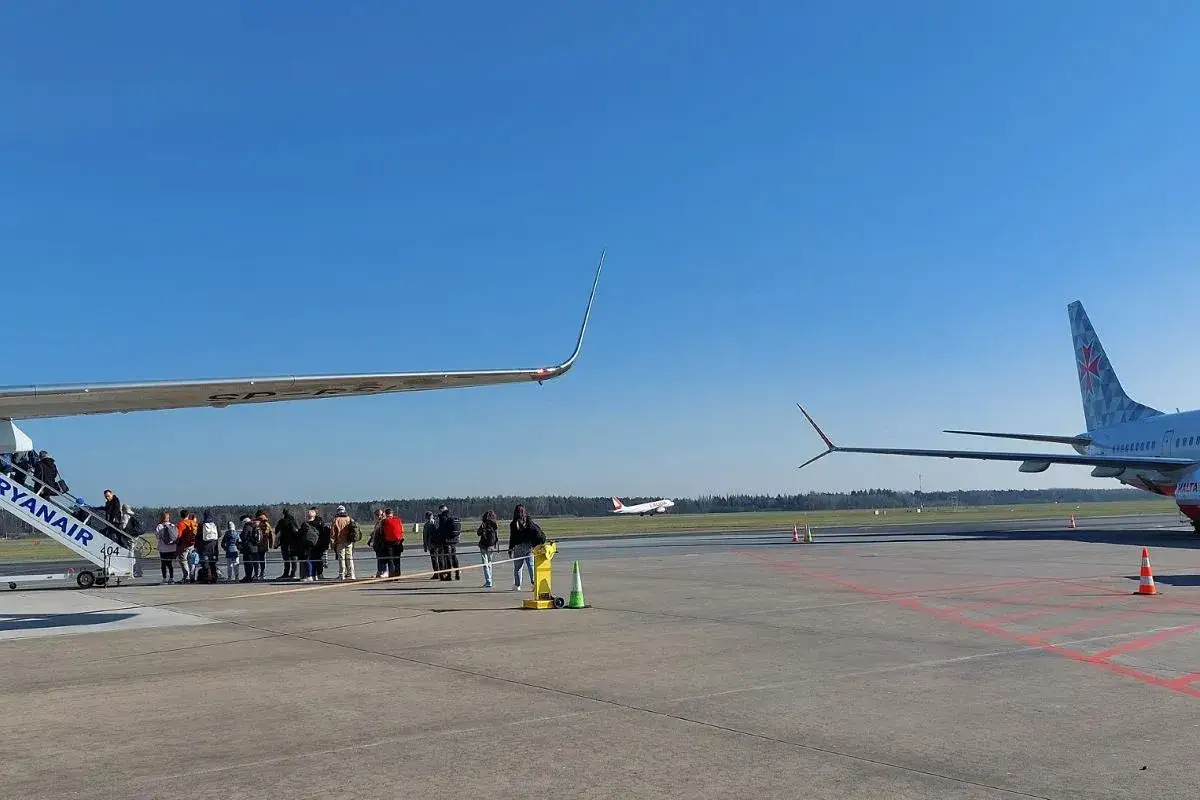 Pasażerowie wsiadają do samolotu Ryanair na lotnisku Modlin. W tle inny samolot startuje.
