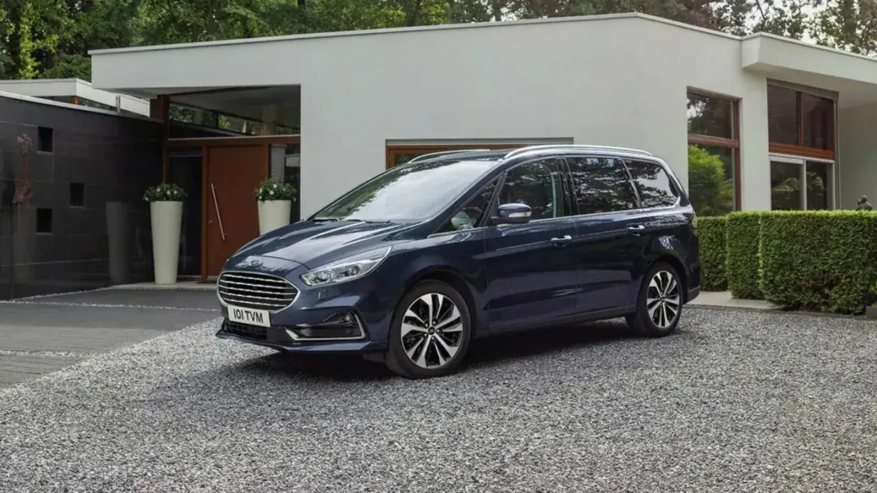 Ford Galaxy azul oscuro aparcado frente a una casa moderna. Las medidas del Ford Galaxy son ideales para familias.
