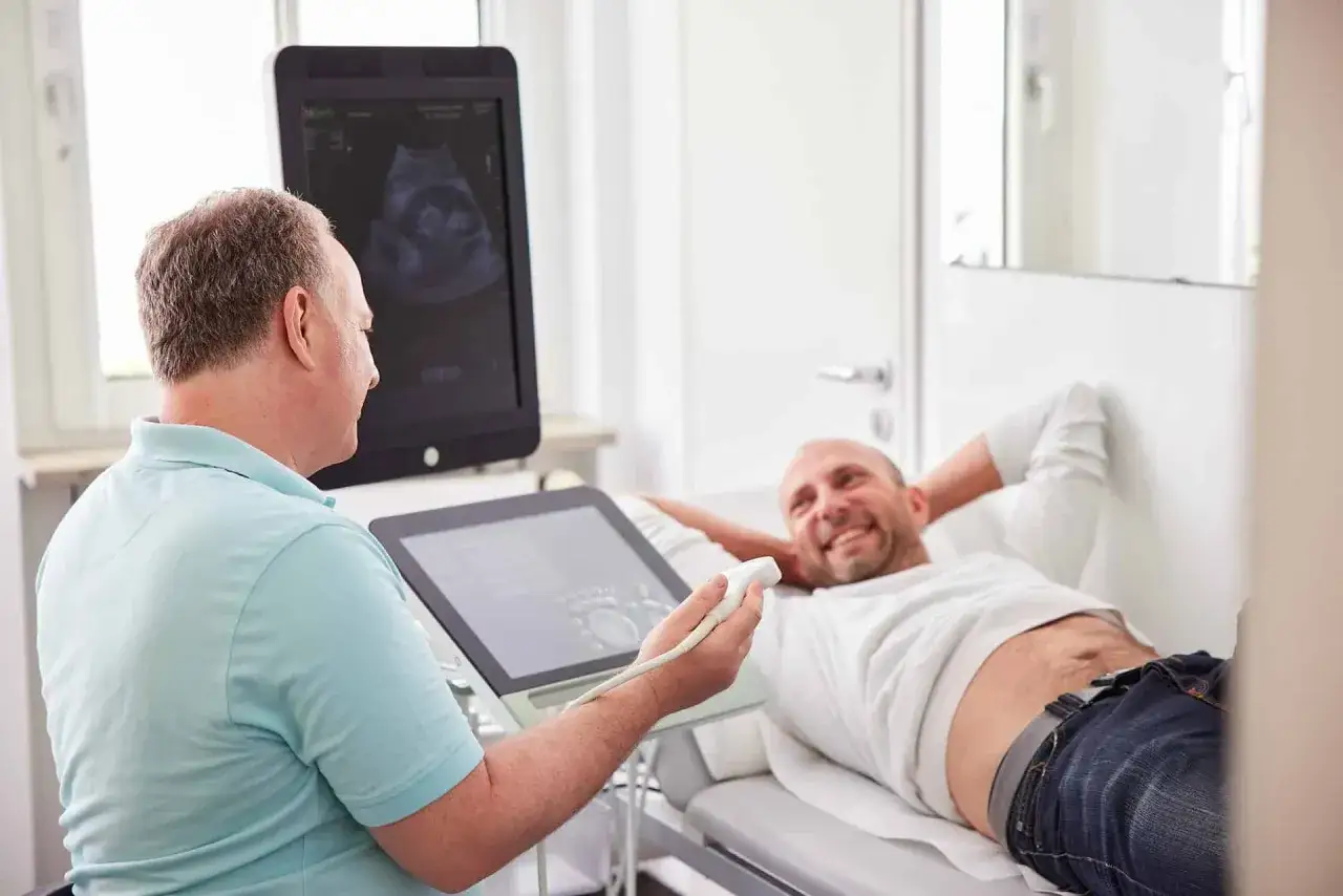 Arzt f&uuml;hrt urologische Untersuchung Mann mit Ultraschall durch. Patient liegt entspannt auf Liege, Arzt bedient Ger&auml;t.