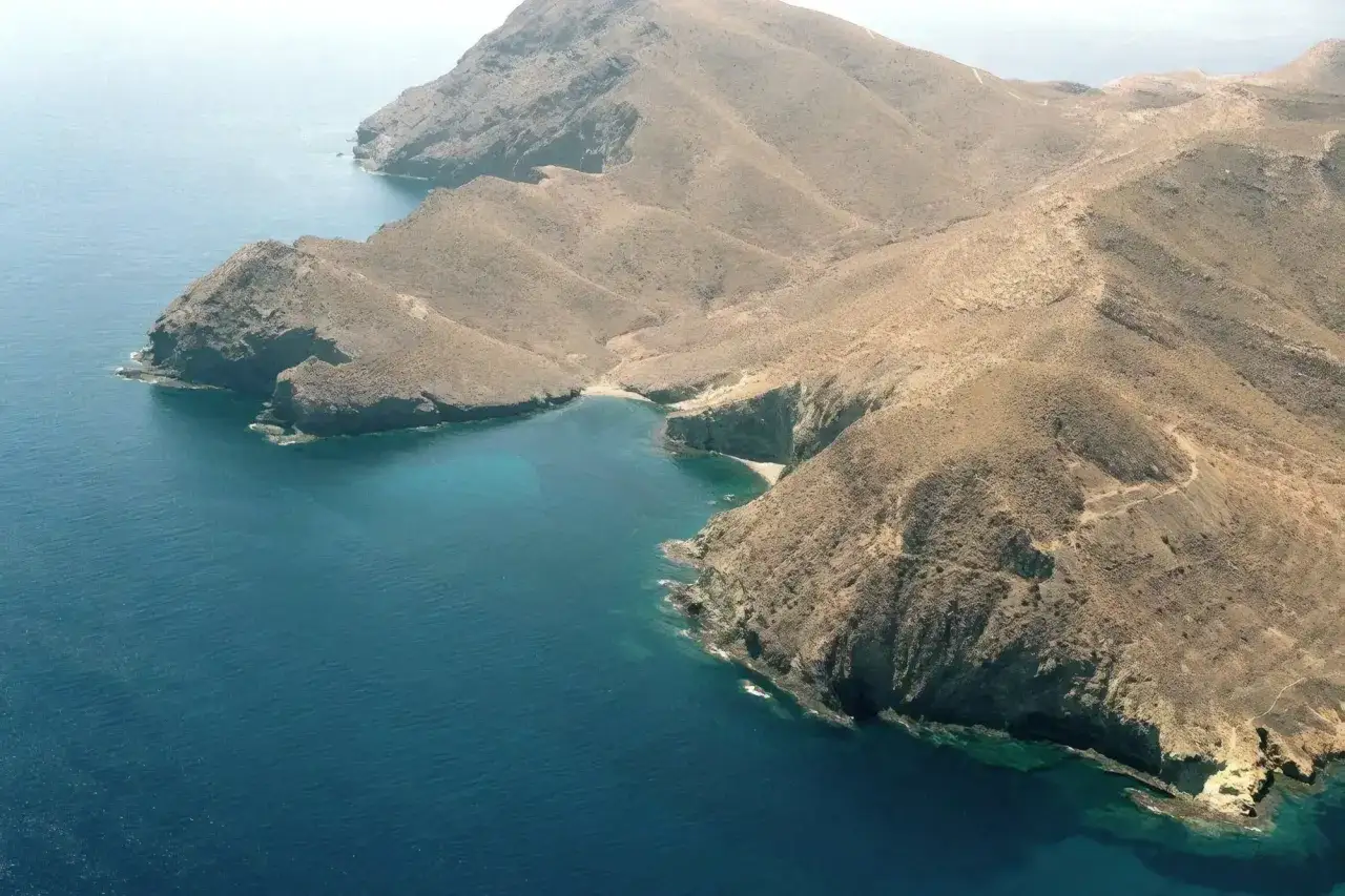 Vista aérea de la cala del bergantín, una bahía de aguas turquesas rodeada de montañas áridas y rocosas.