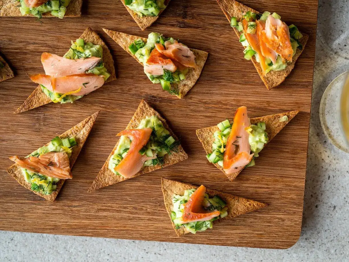 Triangles de crackers garnis de saumon fumé, avocat et concombre. Une recette entrée froide gastronomique facile et élégante.