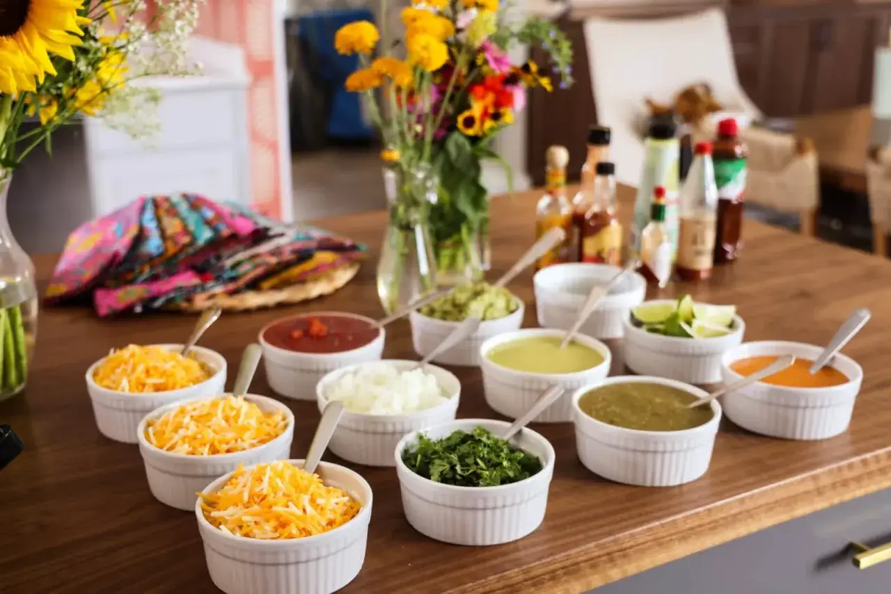 Taco night Vorfreude: Bunte Sch&uuml;sseln mit K&auml;se, Salsa, Guacamole, Zwiebeln und Kr&auml;utern laden zum Belegen ein.
