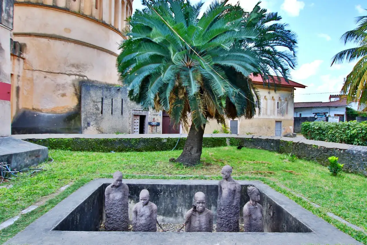 Pomnik upamiętniający zanzibar ludność i jej historię. Rzeźby ludzi w łańcuchach pod palmą.