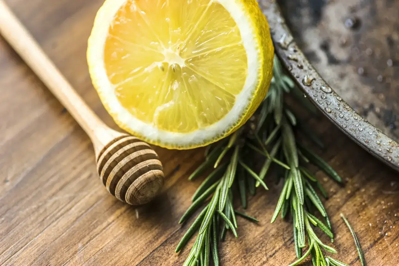 Une tranche de citron, du romarin frais et une cuillère en bois sur une planche. Préparer une infusion romarin citron bienfaits pour la santé.