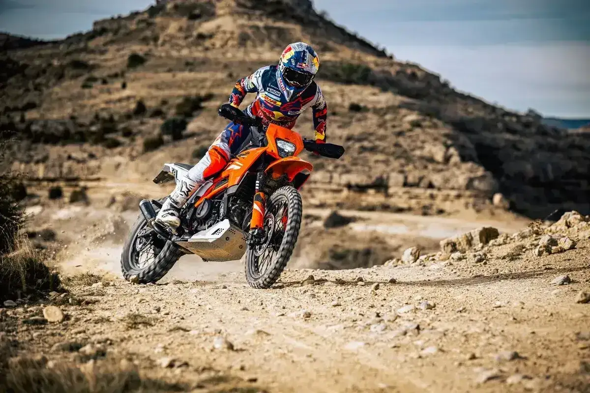 Motocyklista w pełnym rynsztunku śmiga pomarańczowym motocyklem po pustynnym terenie. Czy enduro można jeździć po ulicy? Ten motocykl udowadnia, że tak!