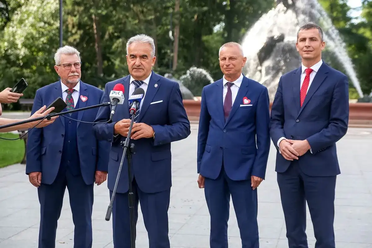 Senatorowie Platformy Obywatelskiej w garniturach, z mikrofonami i telefonami, przed fontanną.