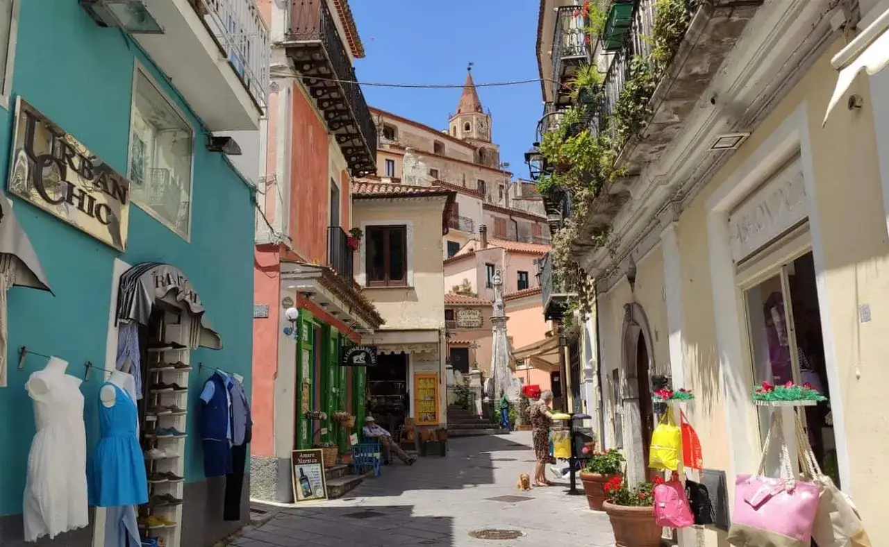 Maratea centro storico cosa vedere: vicoli pittoreschi con negozietti colorati, balconi fioriti e scorci sulla chiesa con campanile.